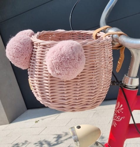 różowy wiklinowy koszyk na rower dla dziecka z pomponami na kierownicę