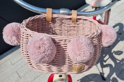 różowy wiklinowy koszyk na rower dla dziecka z pomponami na kierownicę