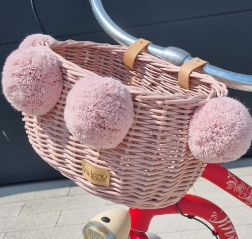 różowy wiklinowy koszyk na rower dla dziecka z pomponami na kierownicę