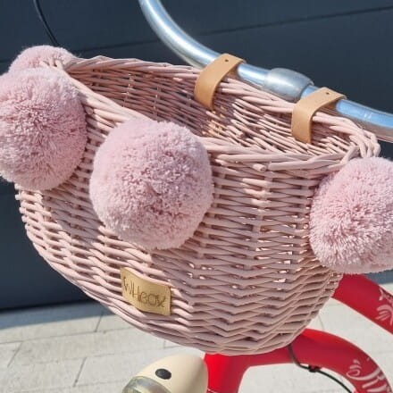 różowy wiklinowy koszyk na rower dla dziecka z pomponami na kierownicę