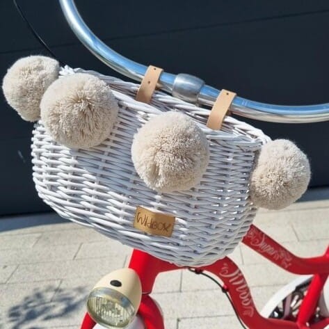 biały wiklinowy koszyk na rower dla dzieci Dumpy w paski z pomponami