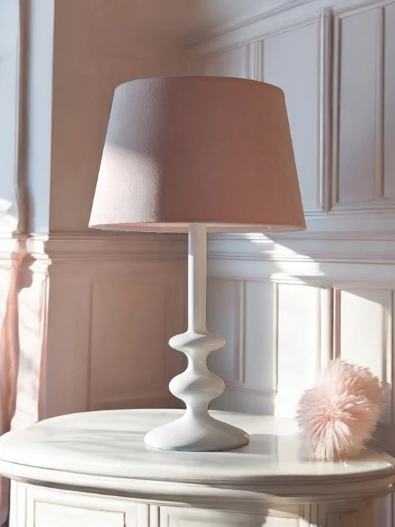 Elegancka-biala-lampa-stolowa-z-ozdobna-podstawa-w-klasycznym-stylu,-z-pudrowo-rozowym-abazurem,-ustawiona-na-jasnej-komodzie-w-przytulnym-wnetrzu-z-panelami-sciennymi.-Idealna-jako-dekoracja-do-salonu,-sypialni-lub-pokoju-dzieciecego.webp