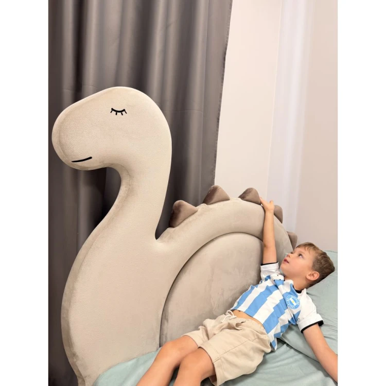 Tapicerowane łóżko dziecięce DINO marki DAPPI z zagłówkiem w kształcie dinozaura i pojemnikiem na pościel.